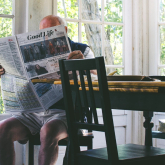 Man sitting at kitchen table reading a newspaper.