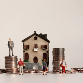 Miniature figures and house along with stacks of coins.