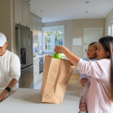Woman holding a child while unpacking groceries at home.