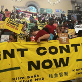 A group standing behind a "Rent Control Now" banner.