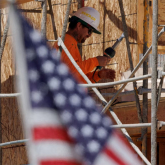 Construction worker on scaffolding with American flag in the foreground.