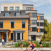 Busy sidewalk in front of a modern multifamily building behind a restored Victorian home.