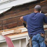 Man on a ladder removing old siding from a home.