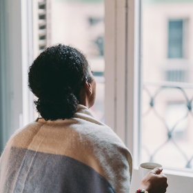 Woman wrapped in shawl staring out of a closed window.
