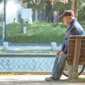 Older man sitting on bench outside.