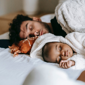 Father and baby napping on bed.