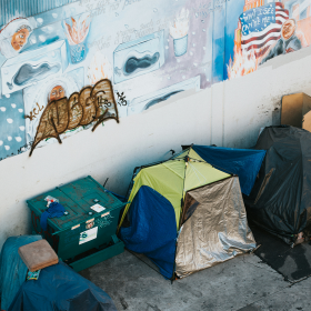 Tents on city sidewalk, with wall mural behind.