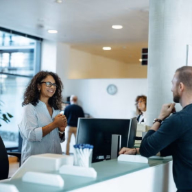 Woman at reception desk welcoming two visitors in an office lobby.
