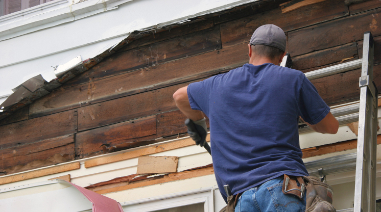 Man on a ladder removing old siding from a home.
