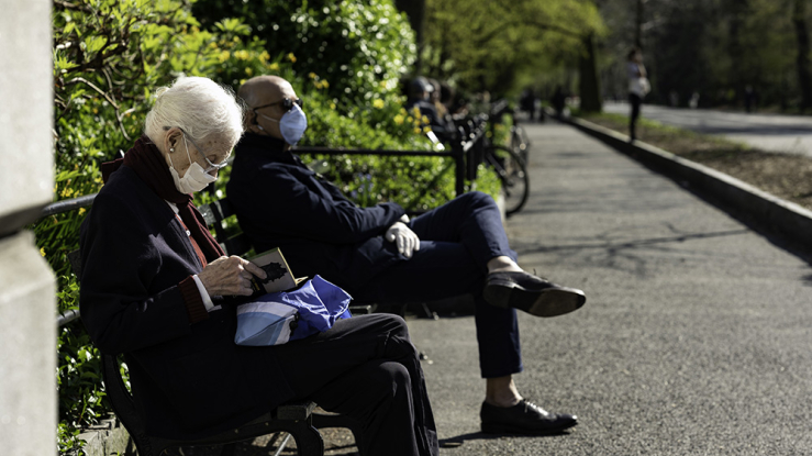 Two older adults sitting on a park bench near sidewalk.