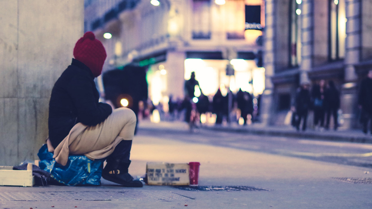 Woman experiencing homelessness sits by the sidewalk.