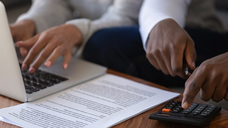 Man and woman calculating information using laptop and calculator.