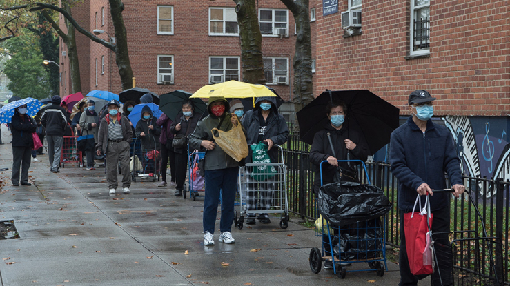 New Yorkers line up in the rain with carts and umbrellas.