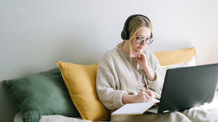 Young woman working on computer on bed.