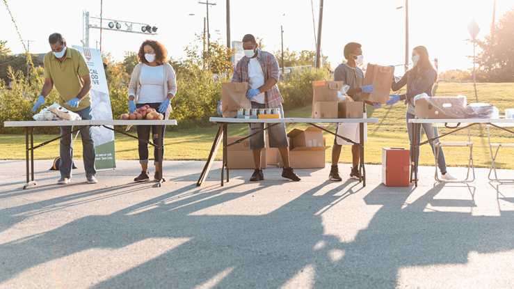 People handing out food at tables outside.