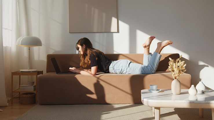 Young woman working on couch in apartment.