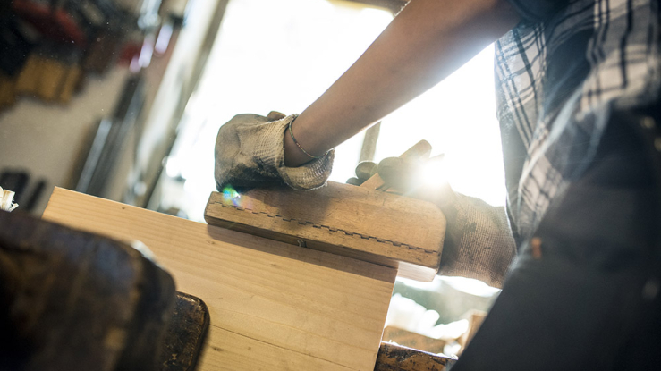 Woman shaping piece of wood in metal clamp.