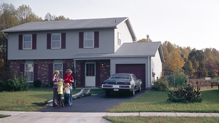 A family stands in the driveway outside their single-family house.