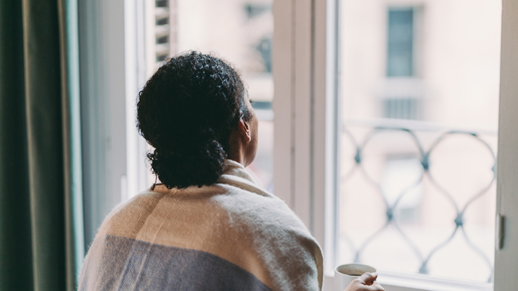 Woman wrapped in shawl staring out of a closed window.