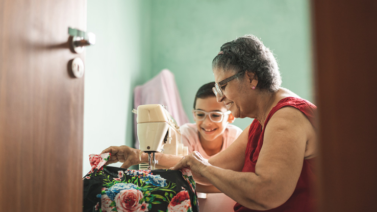 Older woman sewing at sewing machine with young boy watching.
