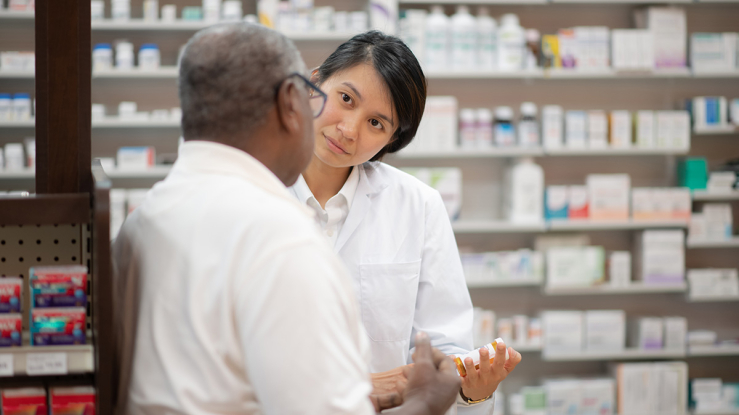 Older man talks to pharmacist while filling prescription.