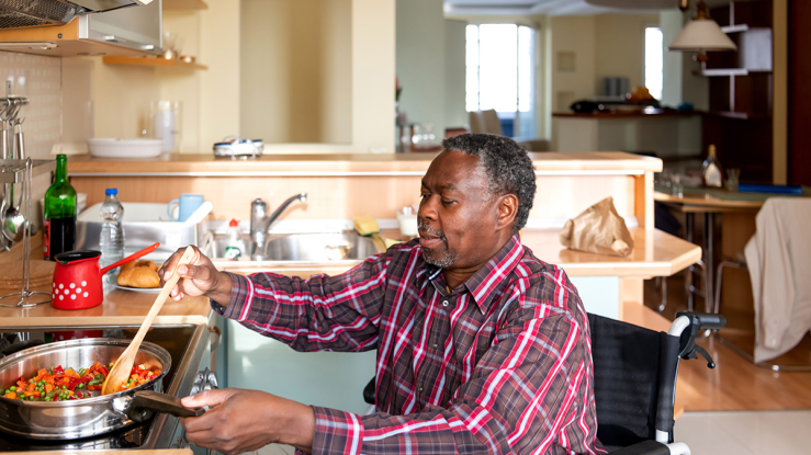 Older man in wheelchair cooking at stovetop.