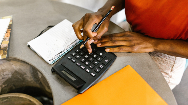 Woman adding up household budget on calculator.