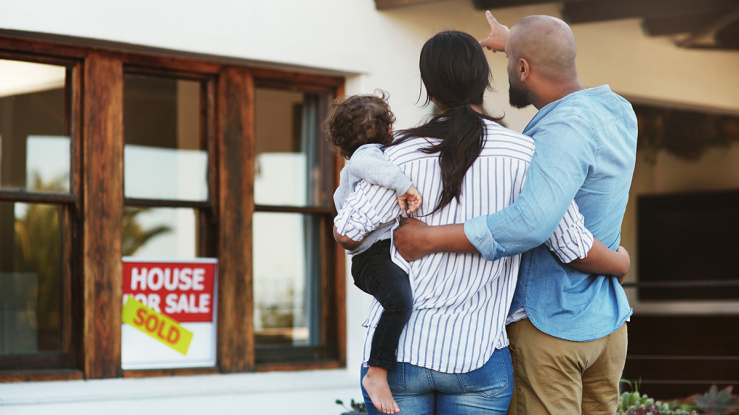Couple with baby looking at house with "sold" sign.