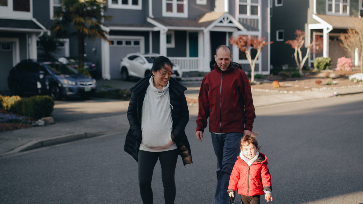 Family walking dog on suburban street.