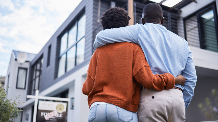 Couple standing together staring up at house.