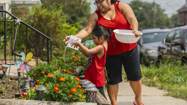 Mother and daughter watering plants in front yard.