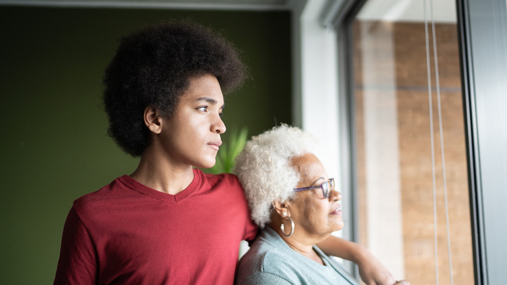 Younger man and older woman standing by window at home.