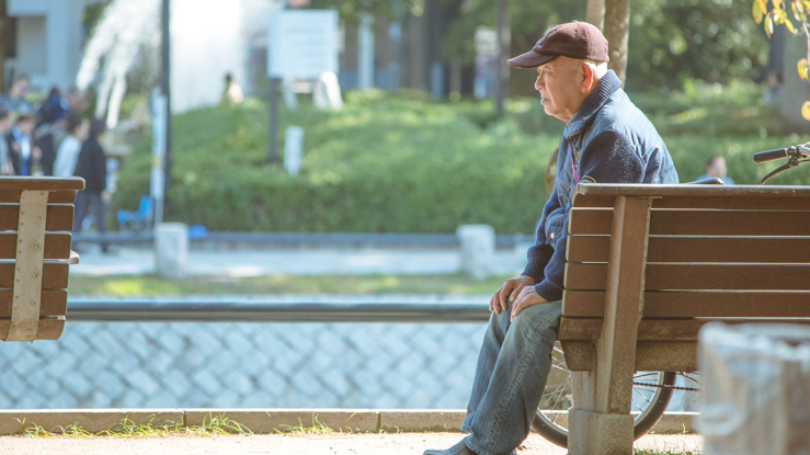 Older man sitting on bench outside.