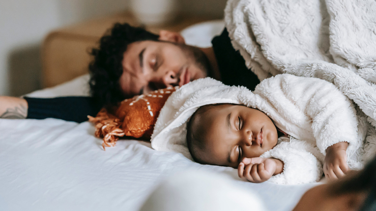 Father and baby napping on bed.