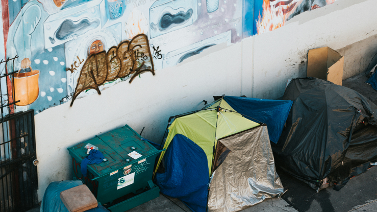 Tents on city sidewalk, with wall mural behind.