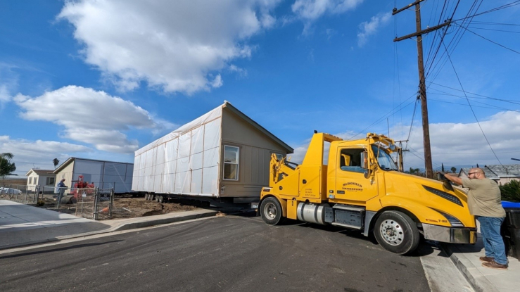 View of a large truck with part of a prefabricated home on the bed.