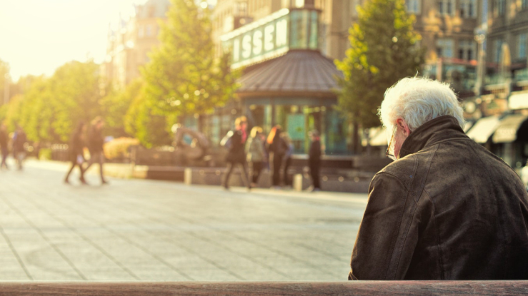 Older man sitting on bench in a public square.