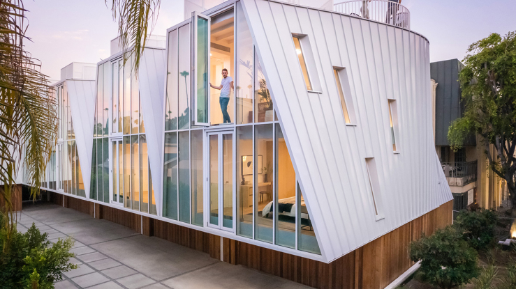 An exterior view of Lorcan O'Herlihy Architects' Canyon Drive development shows a series of four townhouses with inflected roofs and glass facades, all sitting atop private single-car garages clad in wood.