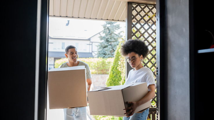 Couple carrying boxes into a house.