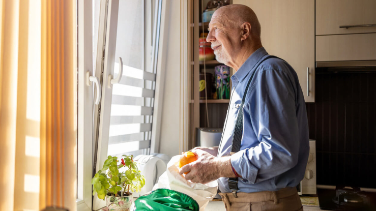 Older adult man looking out kitchen window.