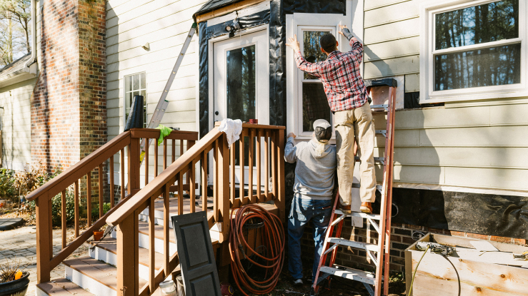Two people outside a house fixing a window