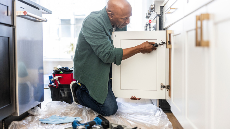 Man installing door on kitchen cabinet.