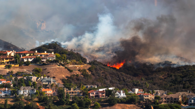 Homes on a hill with wildfire in the background.