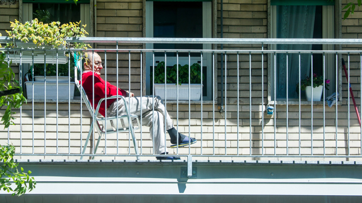Older adult sitting on apartment balcony and looking out at neighborhood.