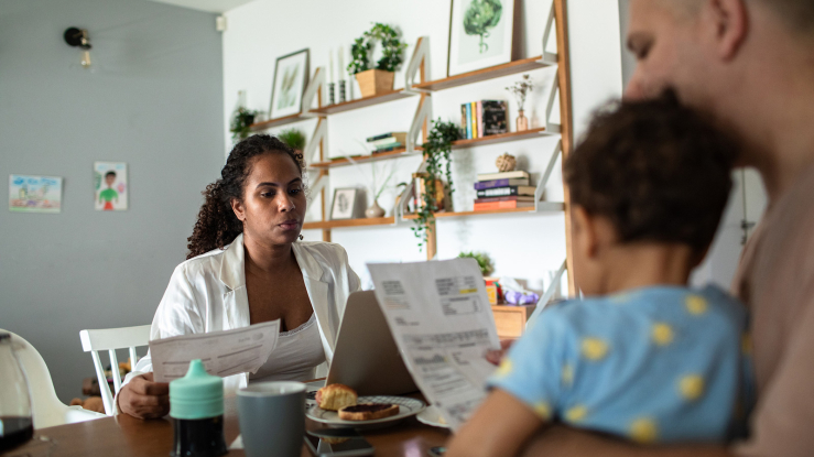Hispanic couple with baby sitting at table reviewing bills.