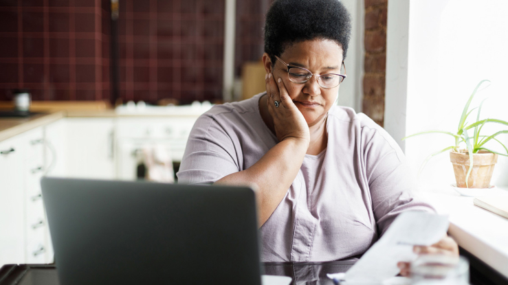 Older adult woman paying bills at kitchen table.