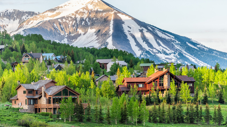 Homes in a wooded area with a snow covered mountain in the background.