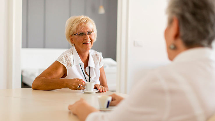 Two older adult woman sitting at kitchen table.