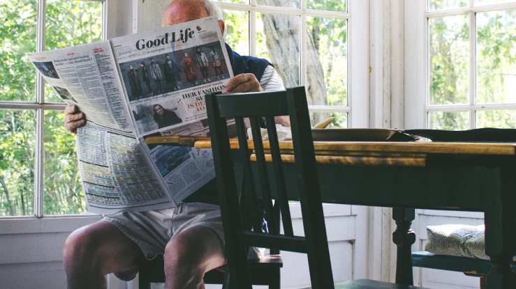 Man sitting at kitchen table reading a newspaper.