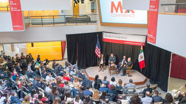 Audience listening to three speakers seated on a stage.